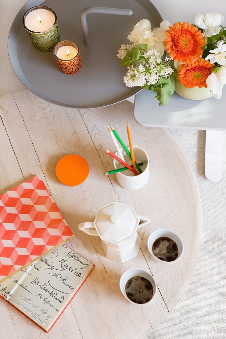 Weiß lasierter Kaffeetisch und Beistelltische aus Metall mit Blumendeko und Windlichtern in Grün und Orange
