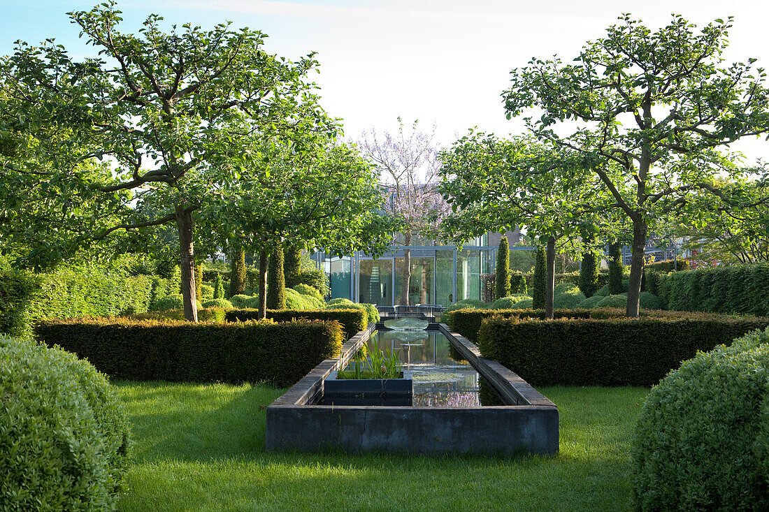 Well-tended, elegant gardens with clipped hedges and concrete pool in sunshine