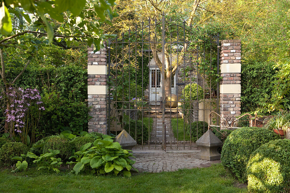 Verstecktes Gartenhaus mit Vintageflair hinter hohem geschlossenem Gartentor und grünem Vorgarten