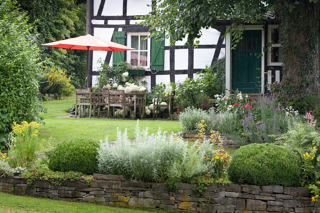Sitzplatz mit Sonnenschirm vor saniertem, altem Fachwerkhaus in idyllischem Garten mit Natursteinmäuerchen