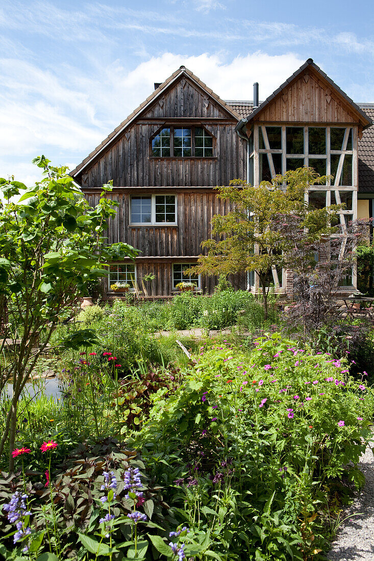 Wilder, blühender Garten vor traditionellem Holzhaus mit mehrstöckigem Erker im Bergischen Land