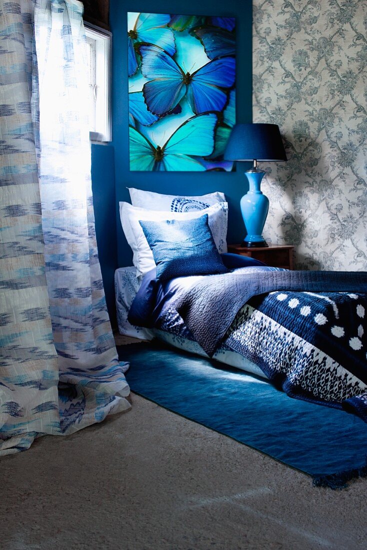 Bett mit Decken und Kissen in Blautönen, darüber Bild mit leuchtend türkisblauen Schmetterlingen