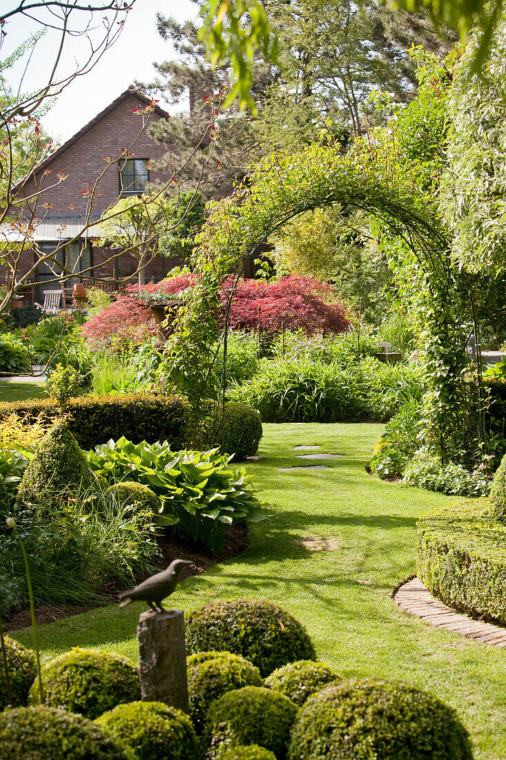 Angelegter Garten mit beranktem Torbogen, im Hintergrund das Wohnhaus