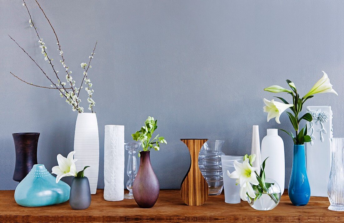 Lilies arranged in vases of various shapes and styles displayed against grey wall