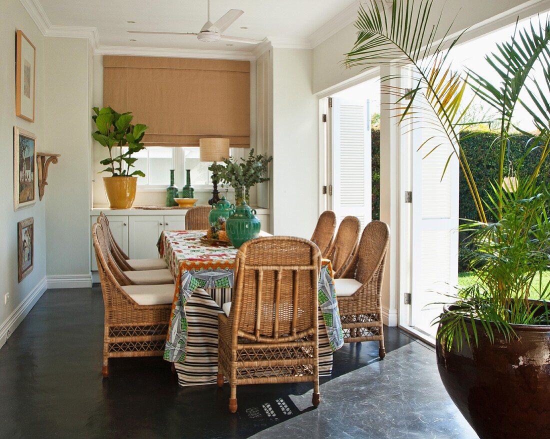 Dining area with wicker chairs and table in front of open shutters on terrace doors leading to garden