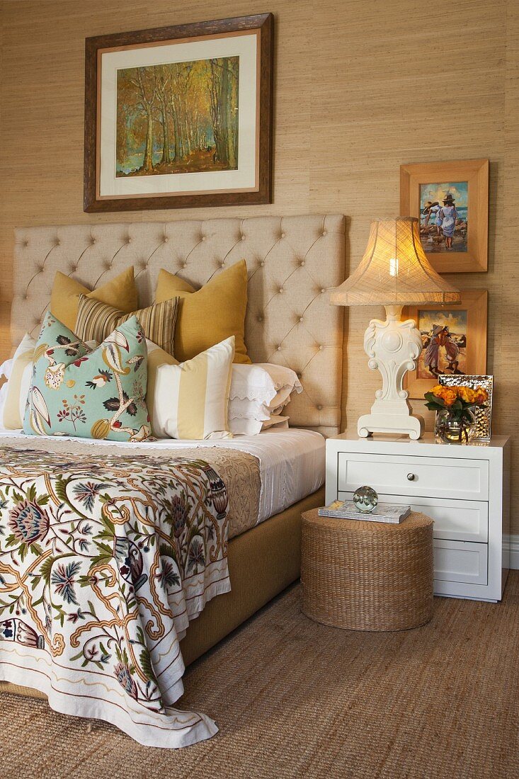 Double bed with beige, quilted headboard flanked by antique bedside lamps on white bedside cabinets