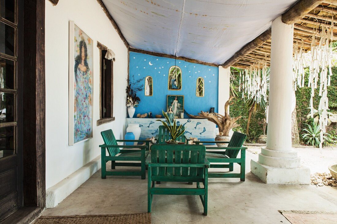 Holzmöbel auf überdachter Terrasse eines brasilianischen Strandhauses mit massiver Tragsäule; Bilder der Meeresgöttin Lemanja mit Altarwand im Hintergrund