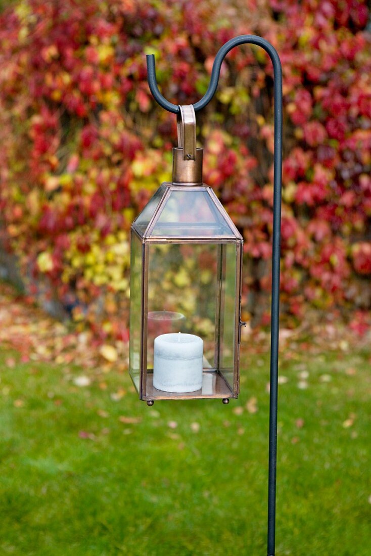 Candle lantern hanging on metal crook in garden