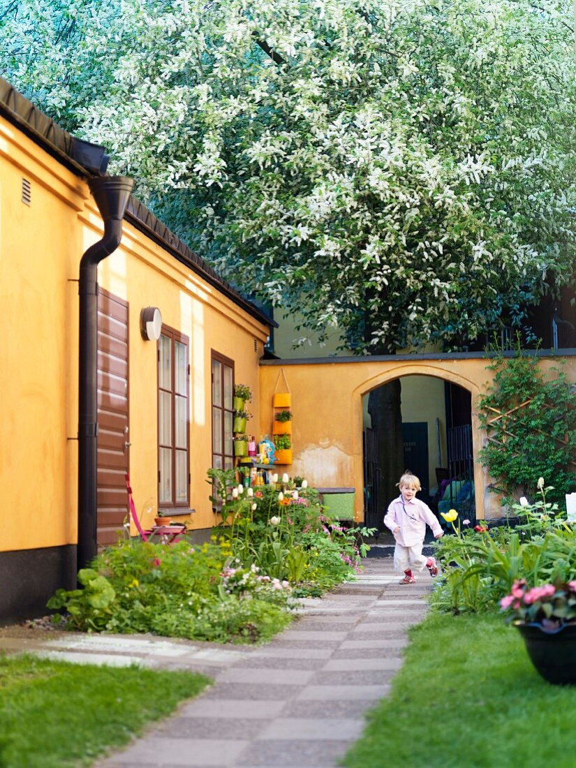 Little boy running through idyllic garden courtyard of Scandinavian bungalow