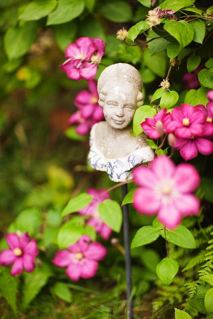 Bust of girl on metal rod amongst pink garden flowers