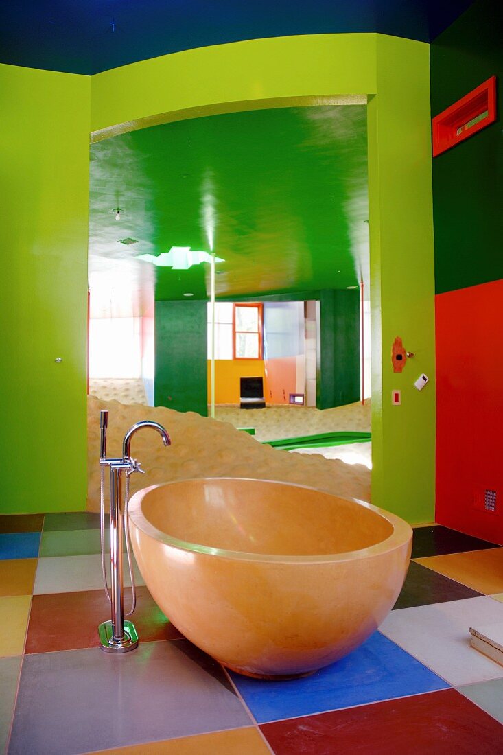 Wände und Decken in kräftigen Grün- und Rottönen; ovale Badewanne frei im Raum auf quadratischen Farbfeldern stehend