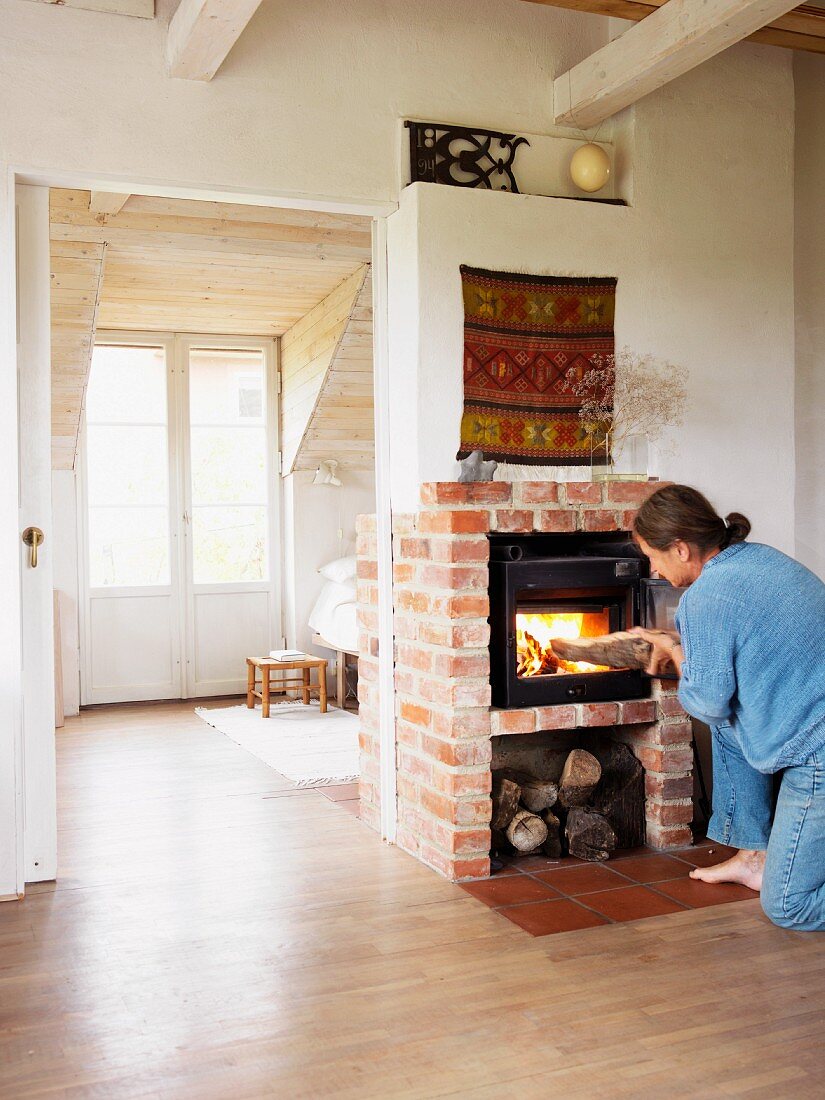 Woman placing log on fire in wood-burning stove