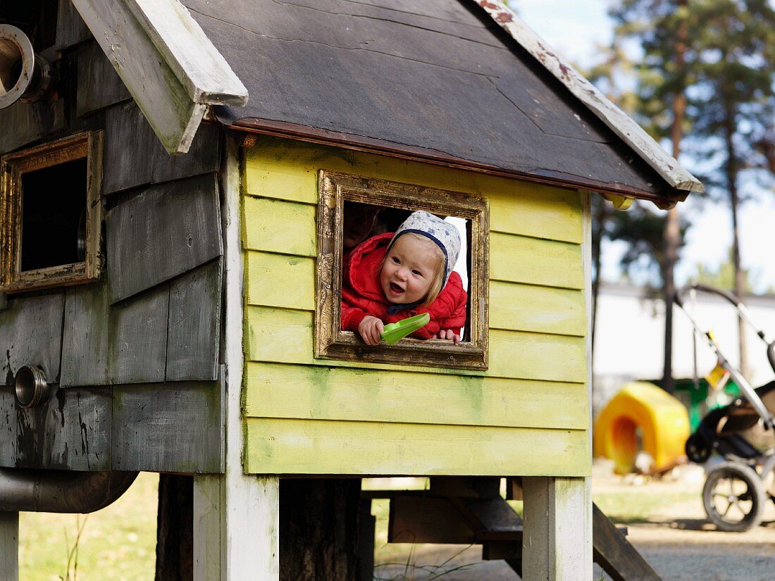 Toddler leaning out of window of wendy house in garden