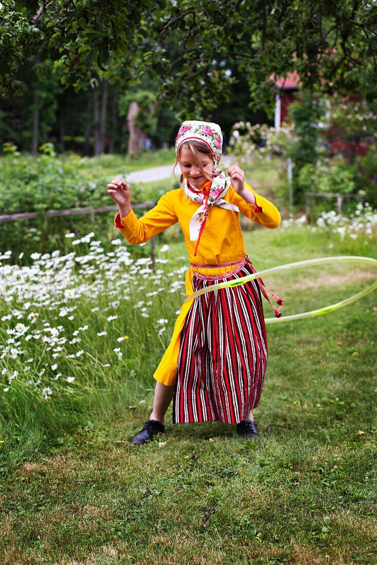 Mädchen in schwedischer Tracht spielt mit Hula Hoop Reifen im Garten