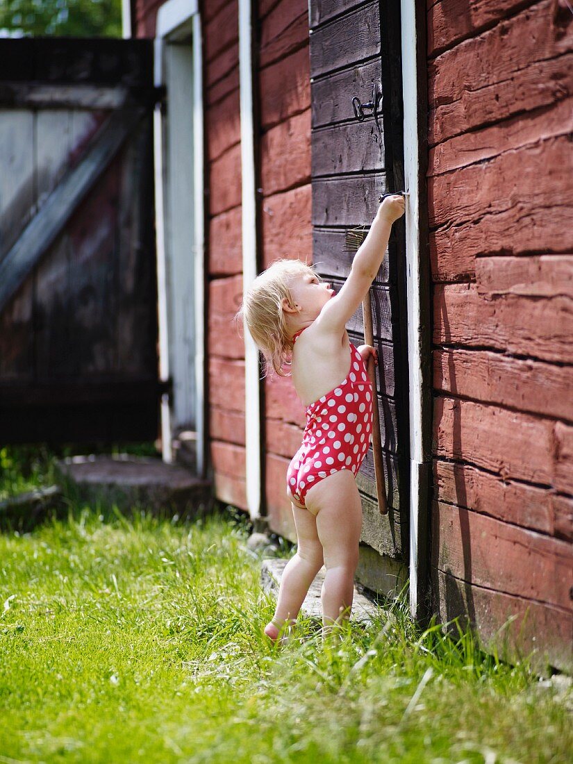 Kleines Mädchen mit Badeanzug im Garten versucht Holztür zu Öffnen