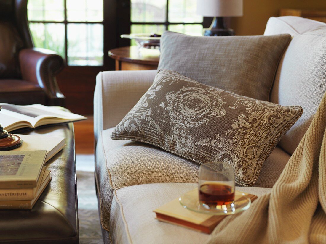 Whiskeyglas und Buch auf Sofa in einem traditionell eingerichteten Wohnzimmer