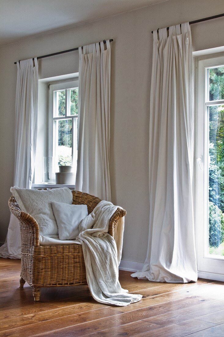 Comfortable wicker chair in front of windows with over-long curtains