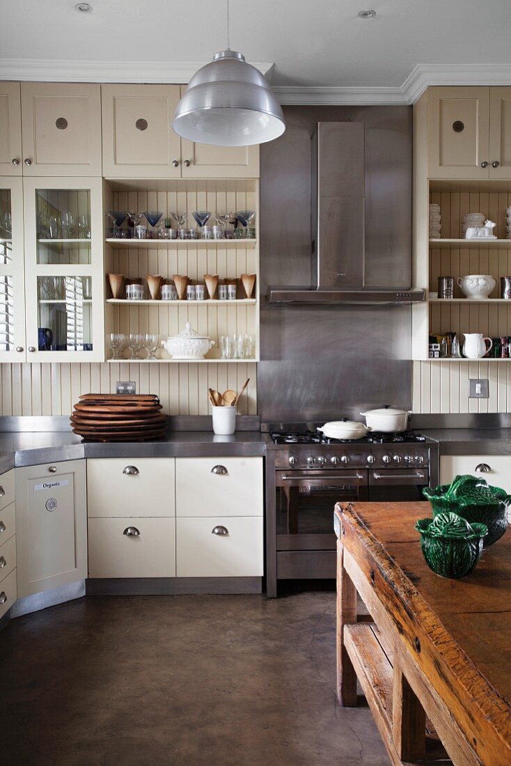 Moderne Landhausküche mit Holz- und Edelstahlfronten; im Vordergrund ein rustikaler Küchenblock aus Holz