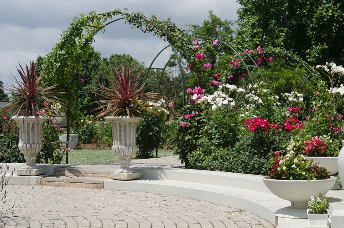 Fürstlicher Garten mit rankenden Rosen; im Vordergrund bepflanzte Steinpokale und -schalen