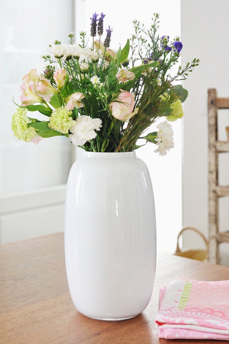 Bouquet of summer flowers with white carnations and lavender in white china vase on wooden table