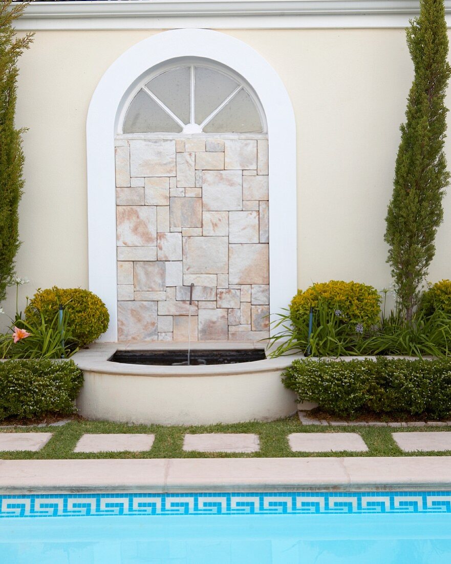 Arched window filled with mosaic of stone tiles and small fountain