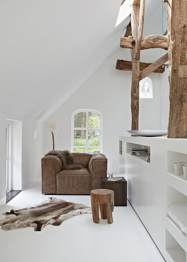 Tasteful leather armchair under sloping ceiling with animal-skin rug on white floor