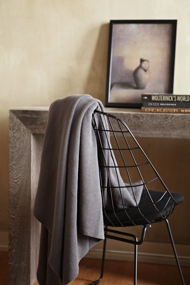 Table made from massive wooden slabs and grey woollen blanket hanging over delicate metal chair