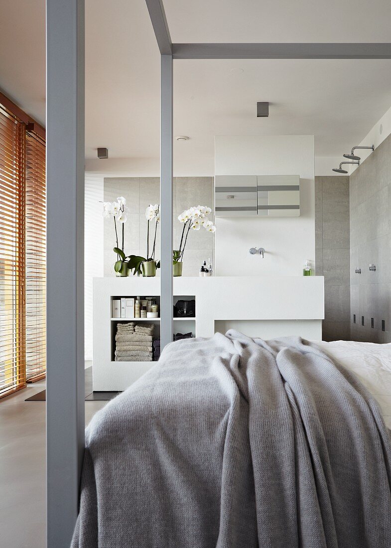 Doppelbett mit grauen Bettpfosten und mit Blick auf den angrenzenden Bade- und Duschbereich mit Brausen