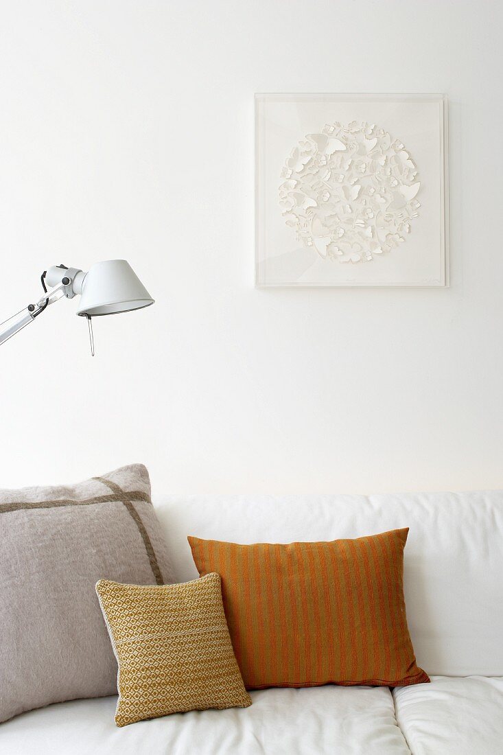 Detail of white couch with scatter cushions in different colours and patterns against white wall