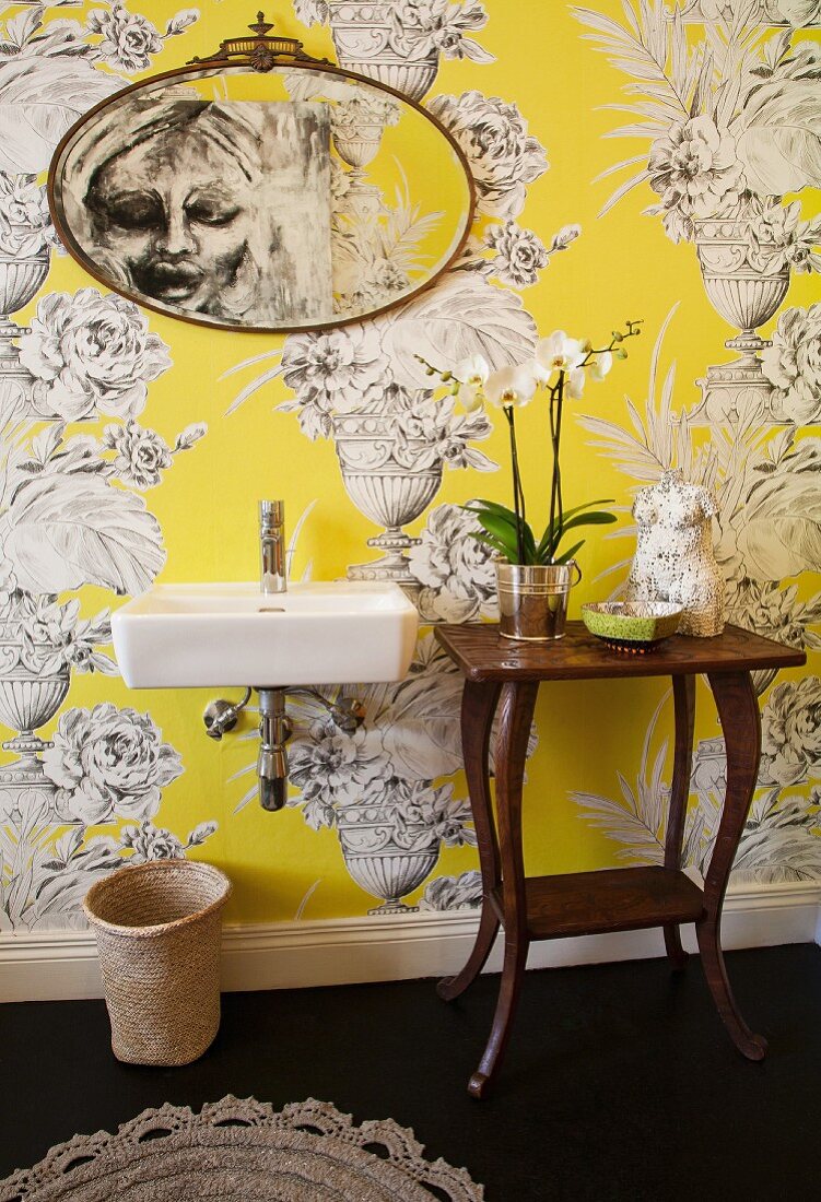 Modern sink and wooden console table with curved legs against yellow wallpaper with large urn motif