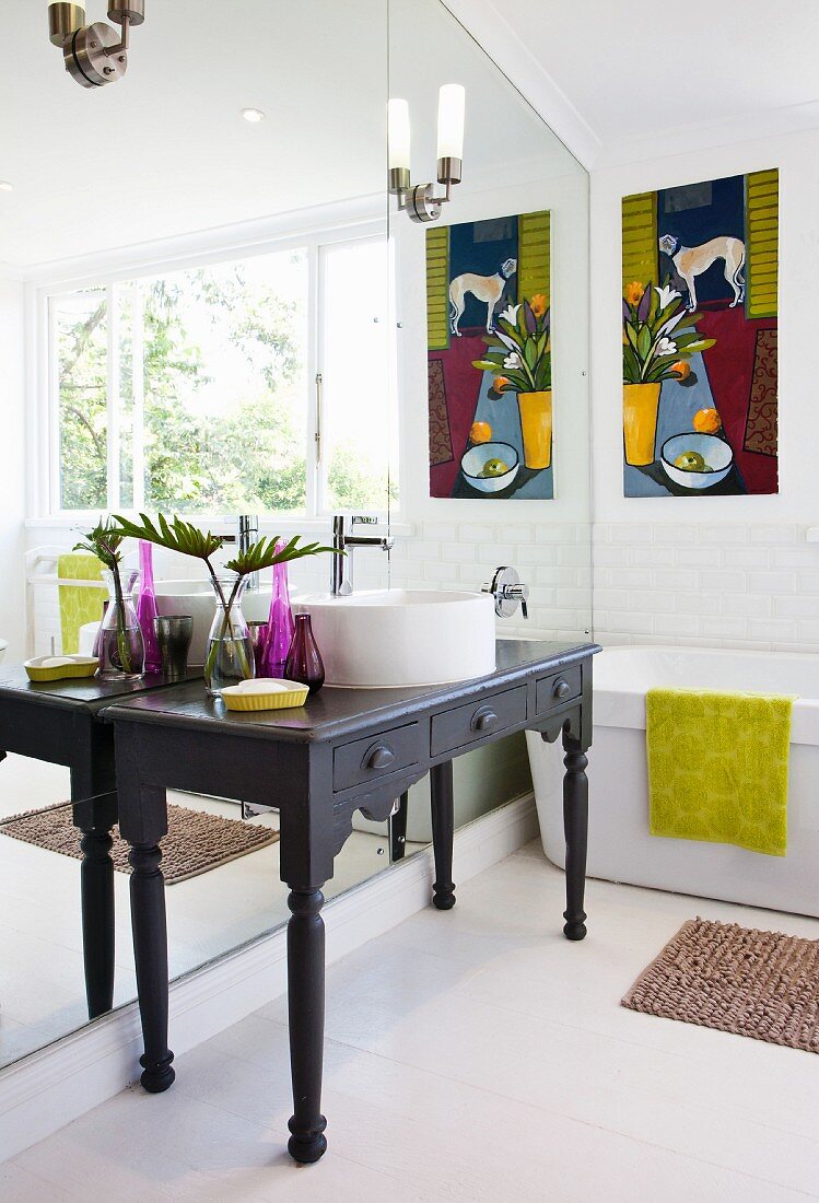 Black-painted console table with carved legs against mirrored wall and bathtub in modern bathroom