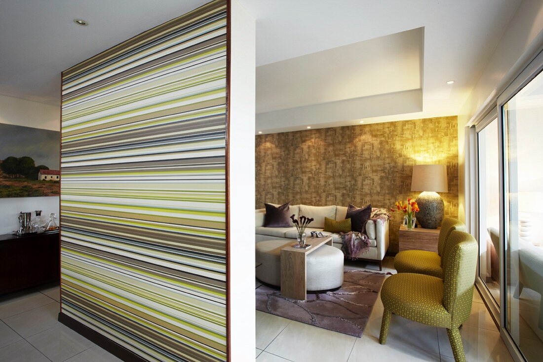 Partition wall with coloured stripes screening lounge with fifties armchairs and modern couch in open-plan interior