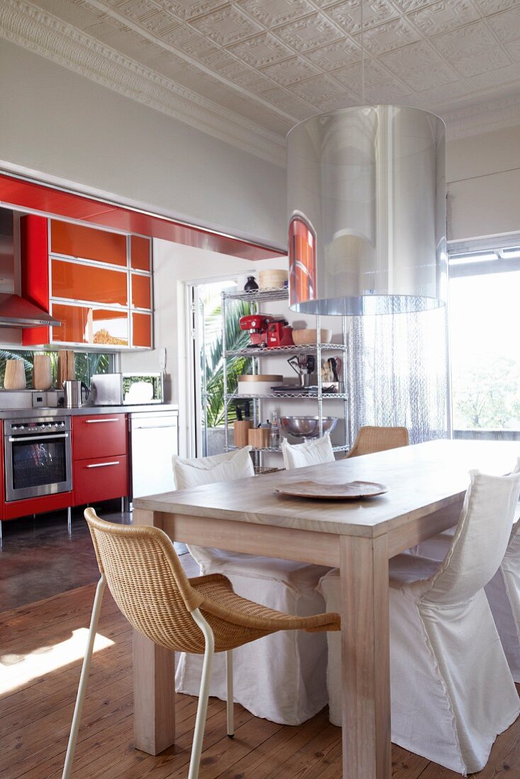 Dining area with modern wooden table and various chairs in front of kitchen with red units