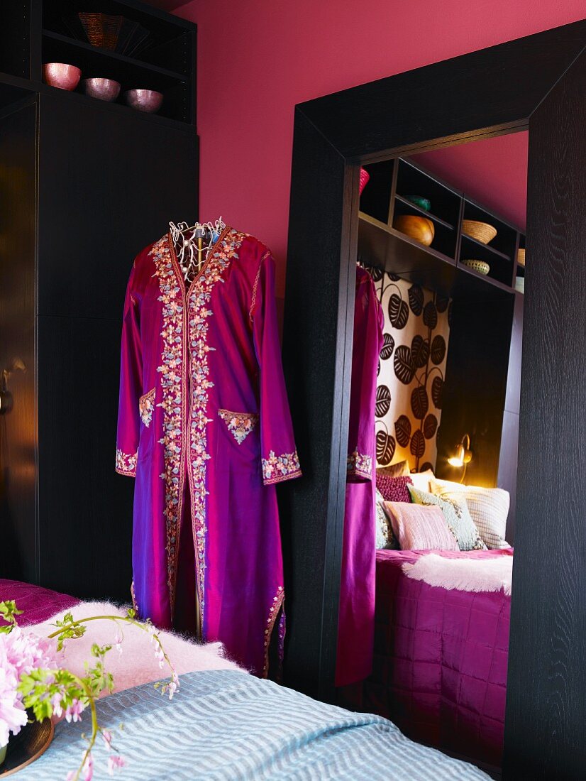 Pinkfarbene Wand mit großem Ganzkörperspiegel; davor eine Modepuppe mit daran hängendem violetten Seidenmantel