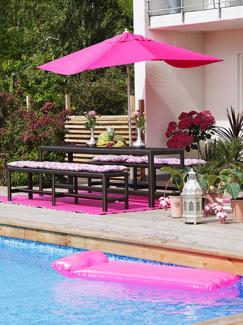 Holzterrasse mit pinkfarbenen Elementen neben azurblauem Swimmingpool