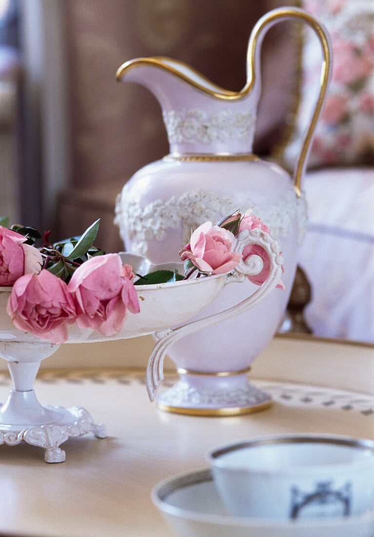 Antiker Krug mit Goldrand neben Etagere mit rosa Rosen