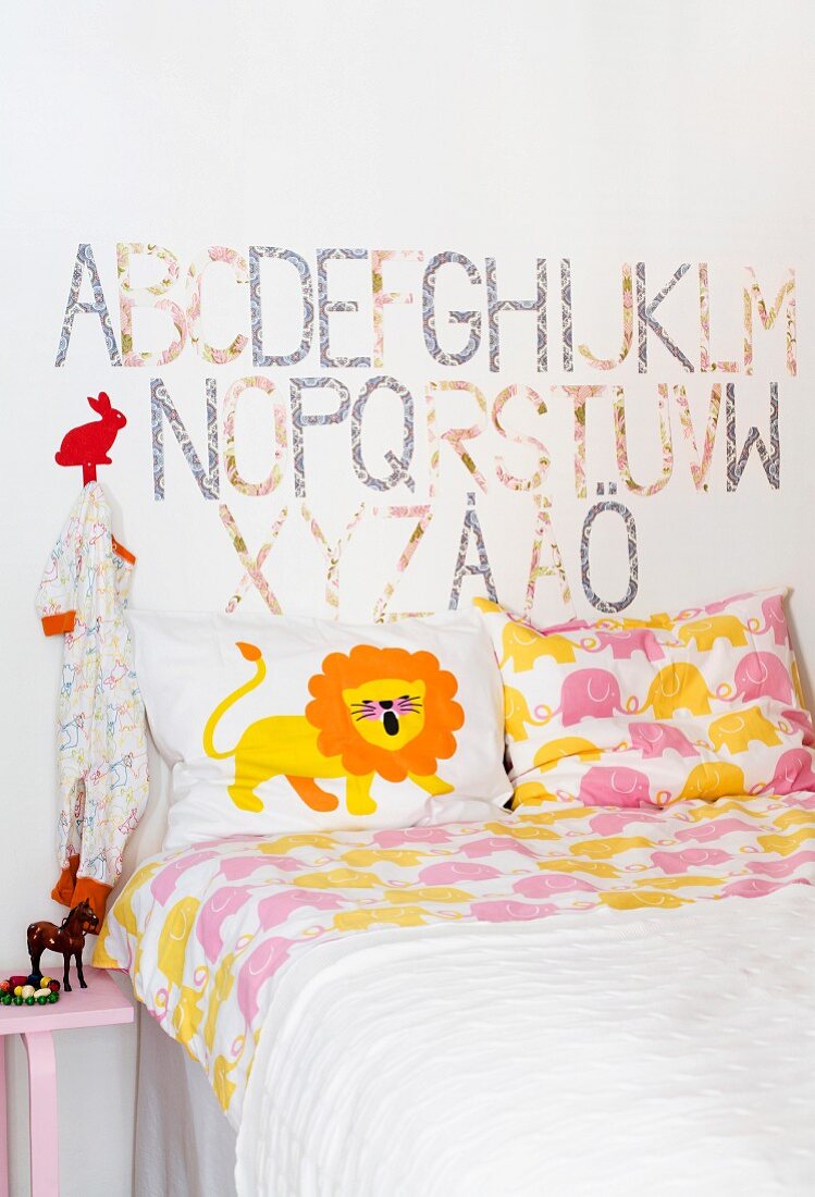 Lustige Bettwäsche mit Tiermotiven in weißem Kinderzimmer; an der Wand das Alphabet und auf dem Nachttisch eine Pferdefigur