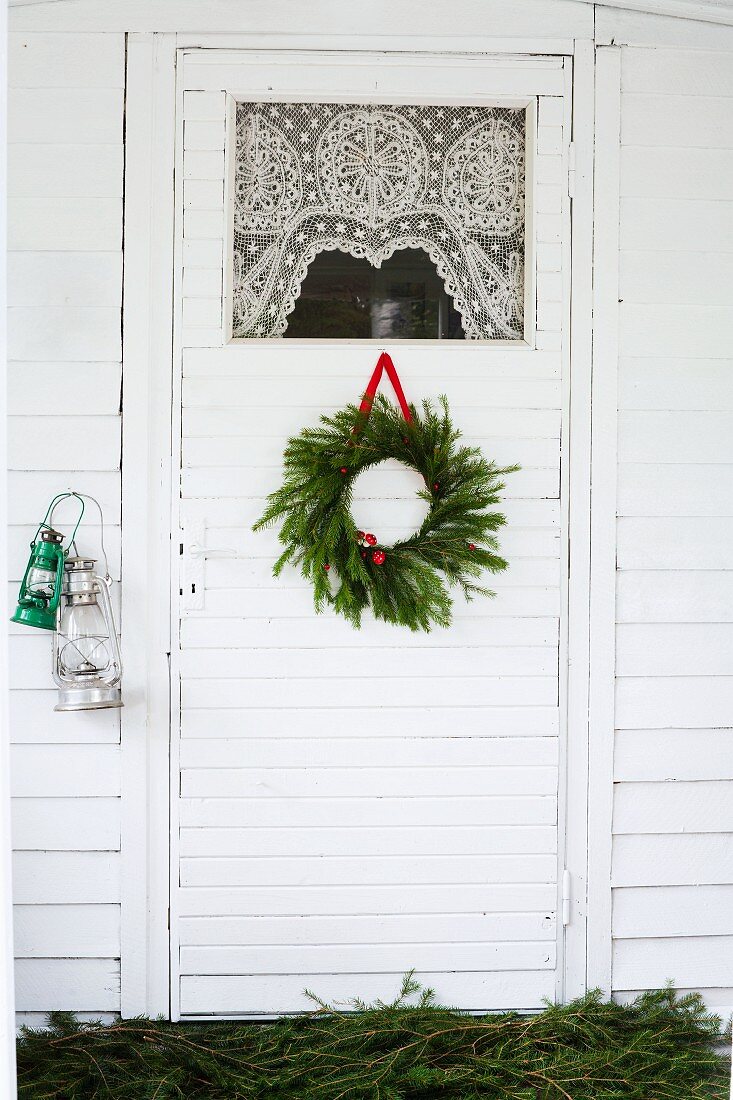 Weihnachtlich dekorierte Tür mit Spitzenvorhang am Glaseinsatz