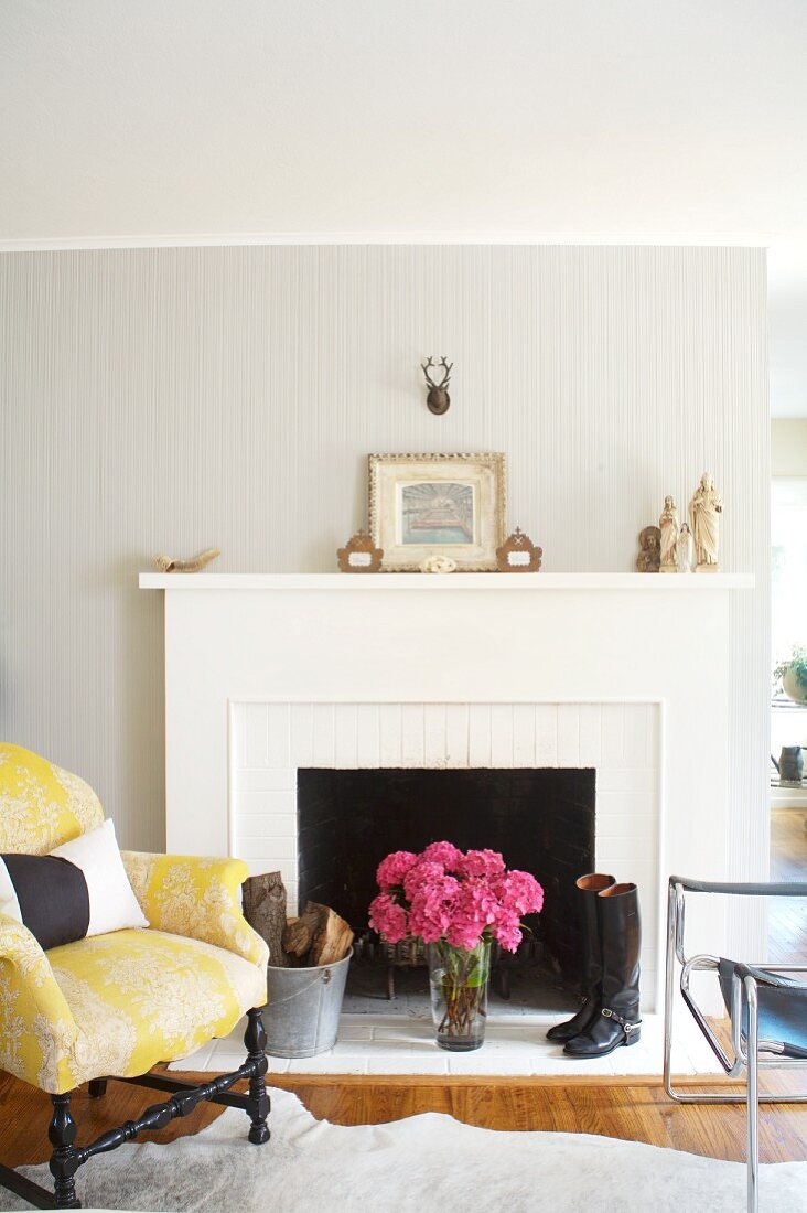 Antique upholstered armchair & modern leather chair in front of open fireplace with white mantel