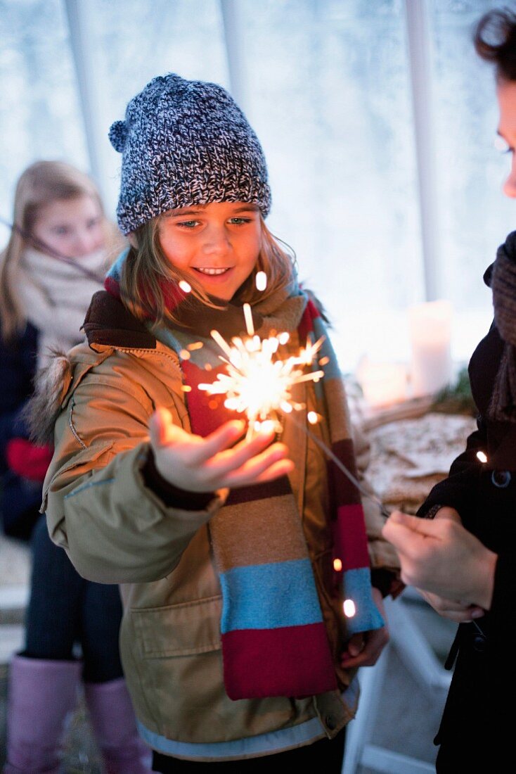 Girl wearing winter clothing looking at sparkler