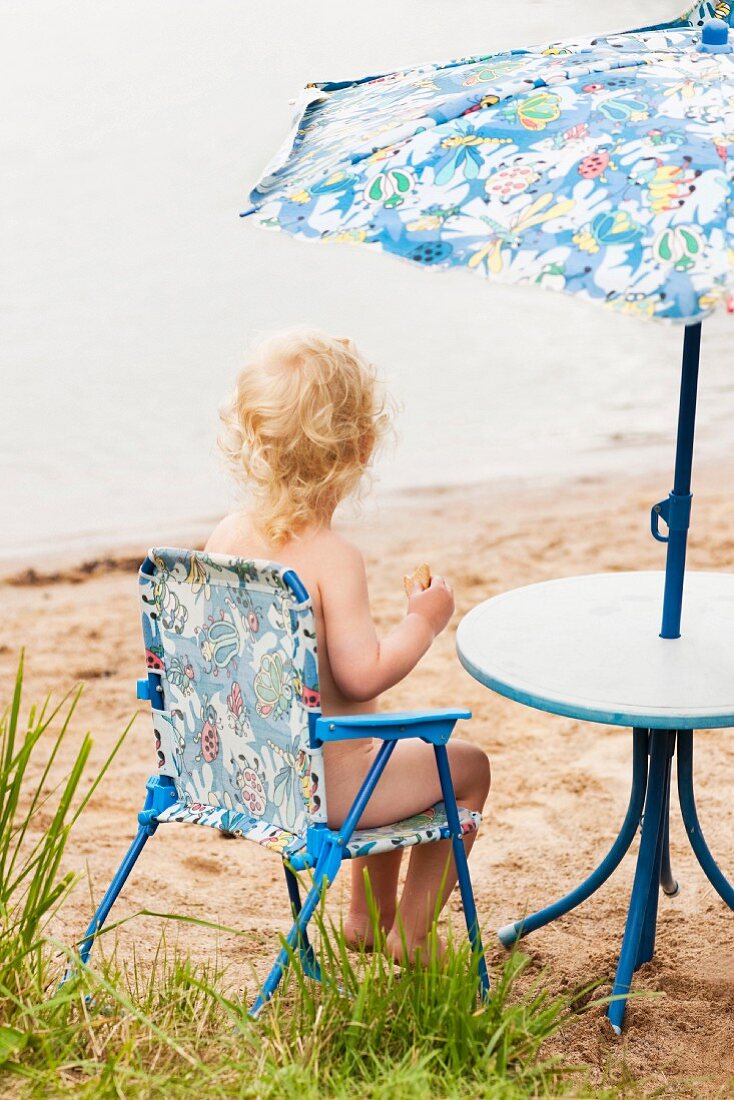 Toddler sitting on camping chair under parasol on beach (Södermanland, Sweden)