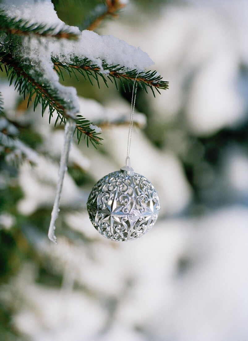 Silberne Weihnachtskugel an schneebedecktem Tannenzweig hängend