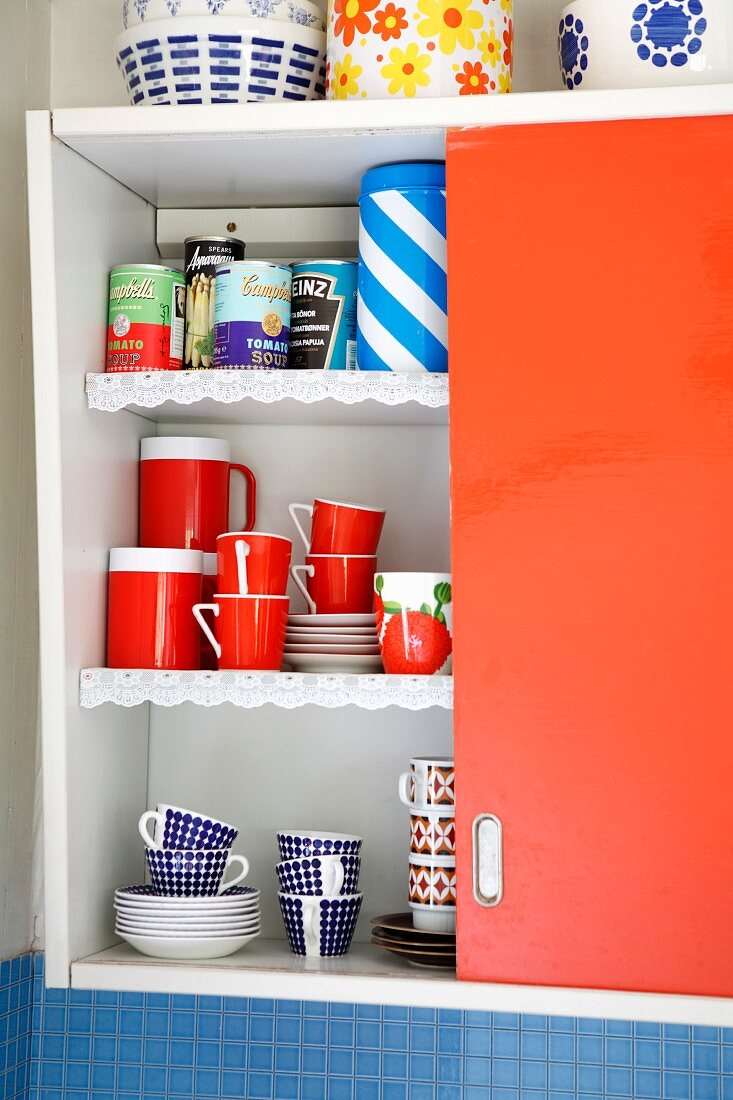 Crockery & groceries in open red kitchen cupboard