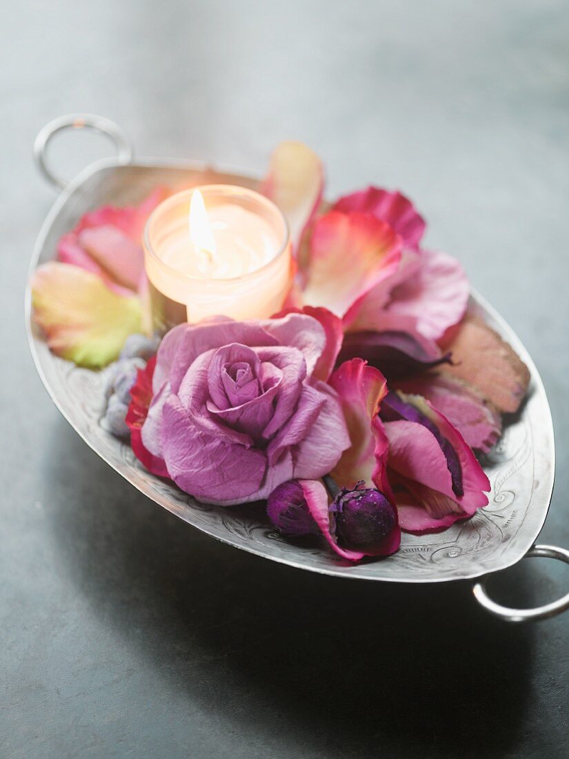 Teelicht mit Blütenblättern und einer Rosenblüte in Silberschale