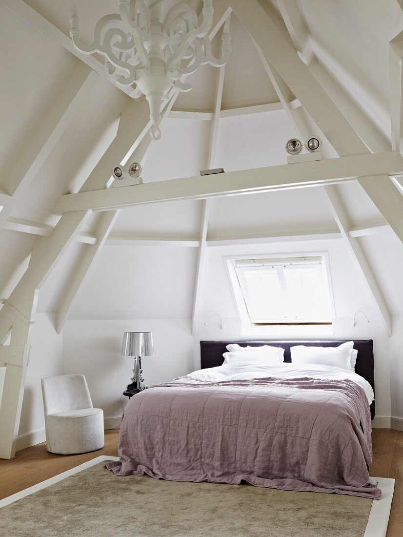 Turmzimmer mit Doppelbett unter dem Dachfenster; auf dem Nachttisch eine Nachttischlampe mit silbernem Lampenschirm