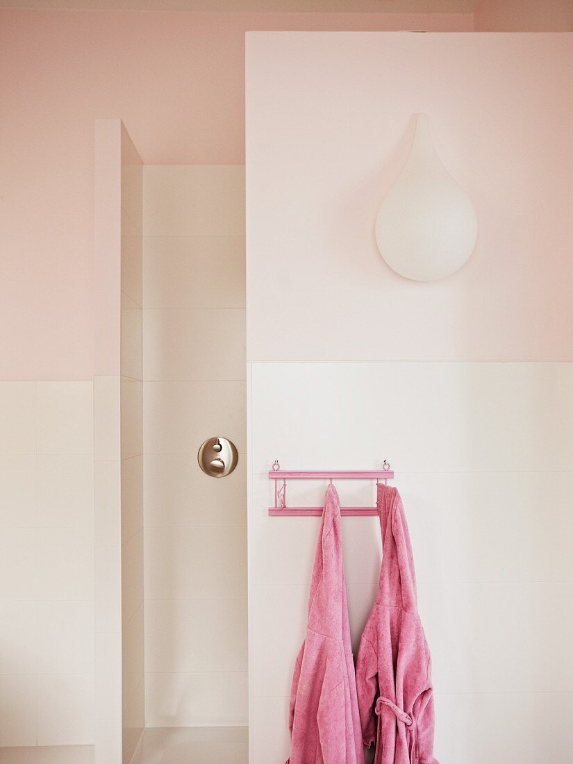 Badezimmer mit tropfenförmiger Wandleuchte an rosa Wand; an einer kleinen Garderobe hängen zwei rosa Kinderbademäntel