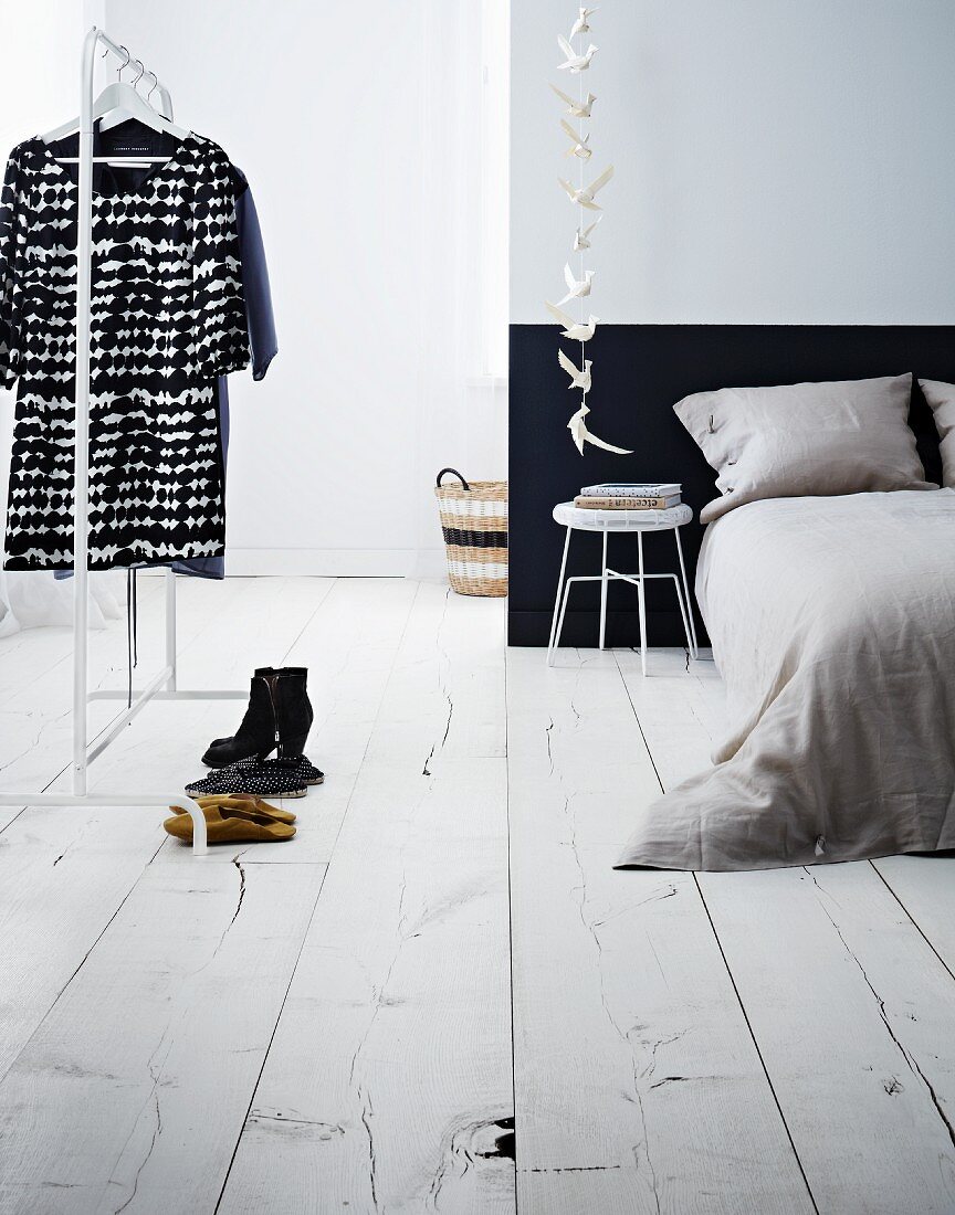 Einfaches, minimalistisches Schlafzimmer mit weißem Holzdielenboden und Kleiderstange mit schwarz-weißem Kleid