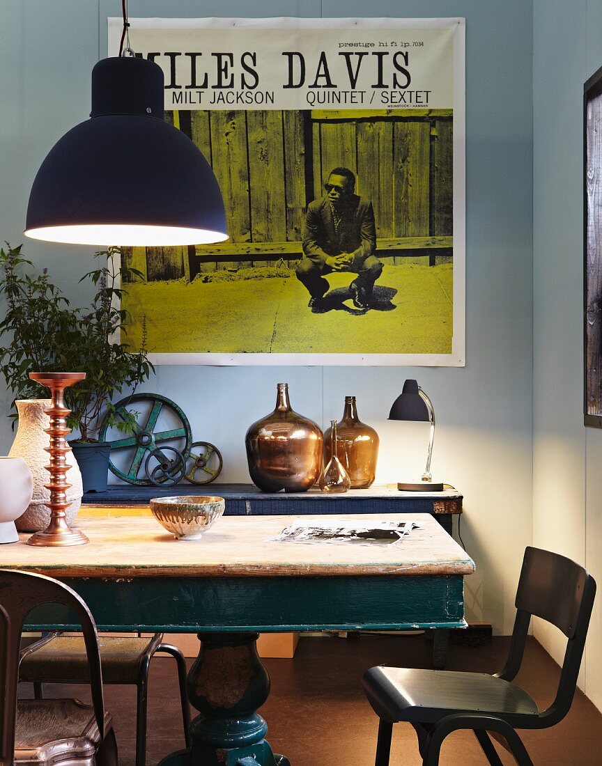 Vintage table and chairs illuminated by large pendant lamp; Miles Davis poster on wall