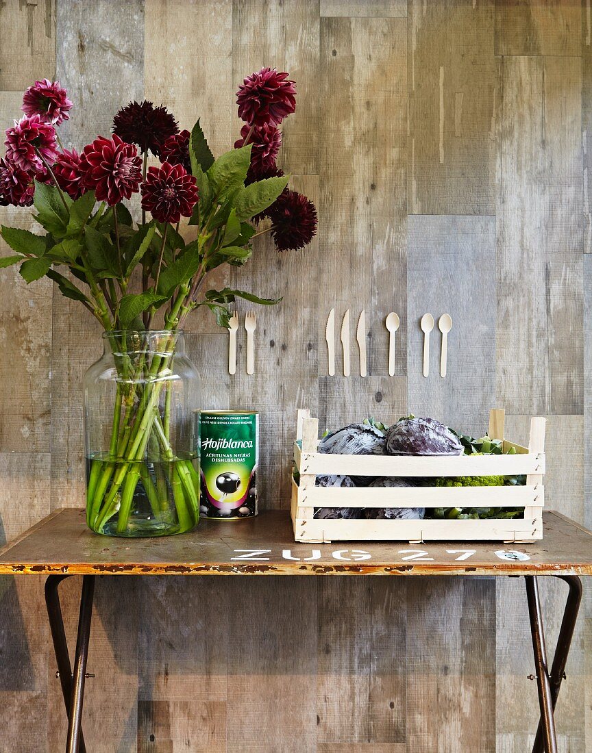 Splendid bouquet of dahlias in glass vase on vintage table against concrete wall with collage of wooden cutlery