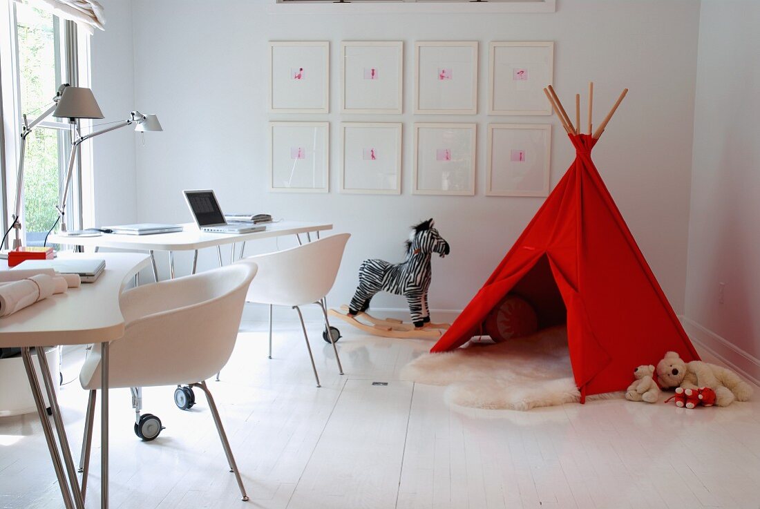 Two workstations with modern shell chairs at desks on castors and toys around red teepee in corner of room